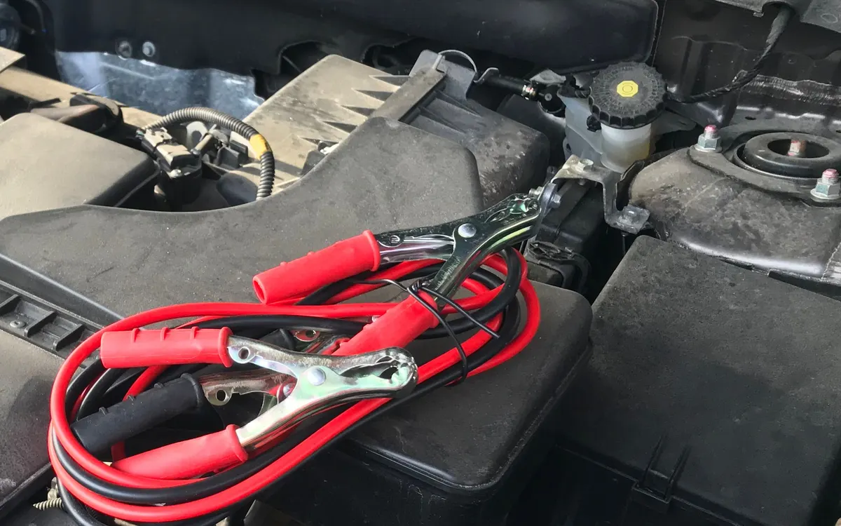 Starthilfekabel im geöffneten Motorraum eines Autos.
