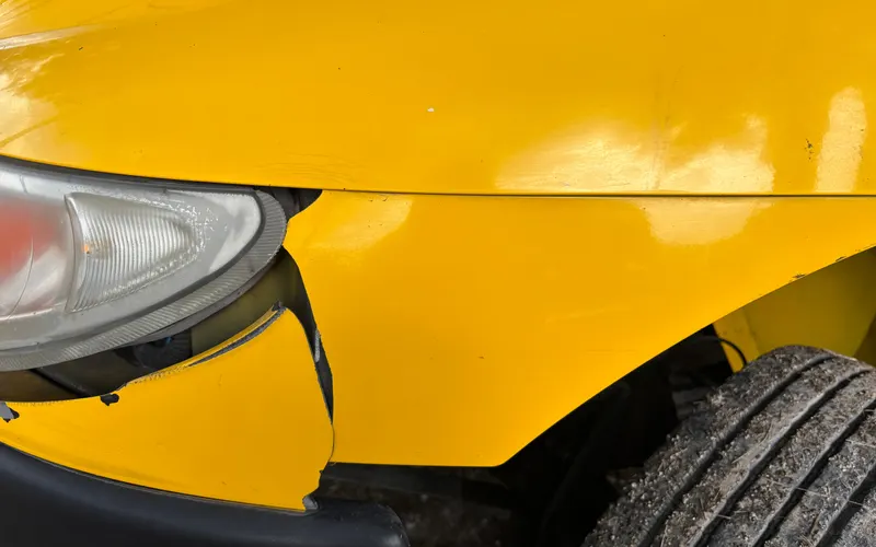 Beschädigte gelbe Frontstoßstange unter einem Scheinwerfer.